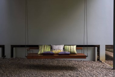 Uzun ahşap açık salıncak tezgah yastıklar, çakıl zemin ve gri Duvar ile.