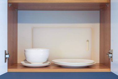 Beyaz tabaklar, kaseler ve kesme tahtası olan metal kapak Menteşe ahşap mutfak dolabında