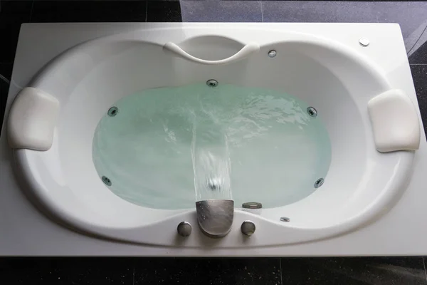 Empty white massaging jetted bathtub on black polished stone floor — Stock Photo, Image