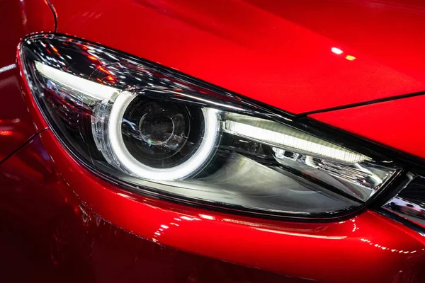 White headlight of red car with front hood and bumper