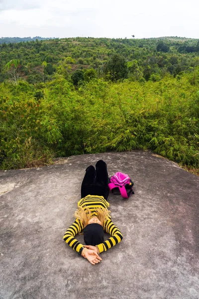 Asian woman lying on rock cliff with mountain background