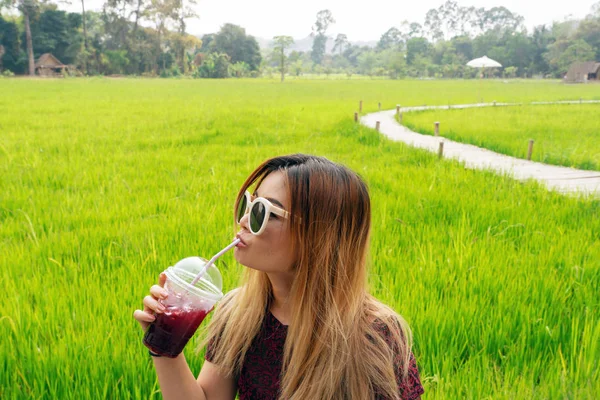 Asian woman drinking red juice with rice field background