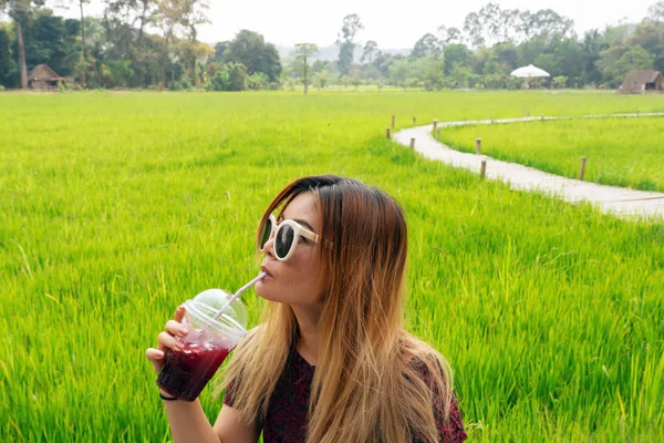 亚洲妇女喝红果汁与绿色稻田背景 — 图库照片