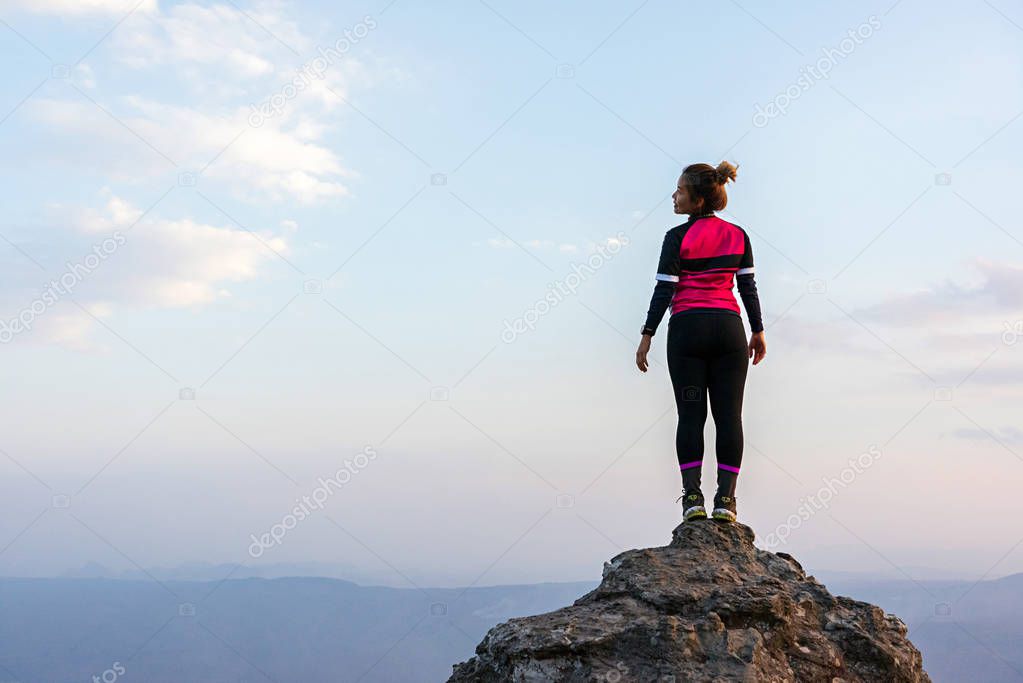 Asian woman in pink sportswear standing on rock cliff