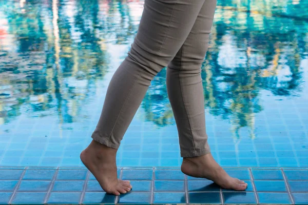 Female legs walking on poolside with trees reflection on pool