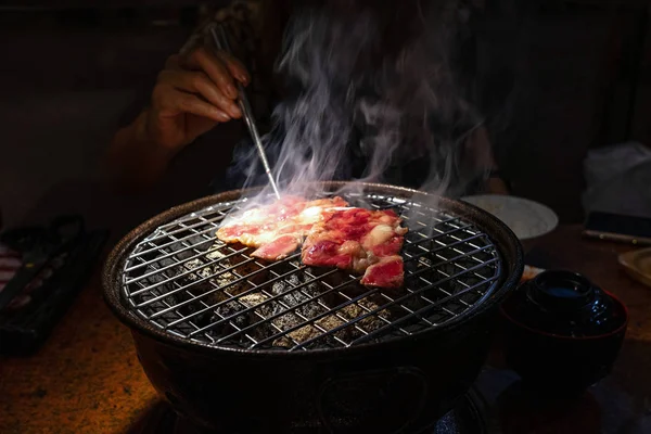 Carne di manzo cruda rossa sulla griglia a carbone con bacchette che tengono in mano Foto Stock Royalty Free