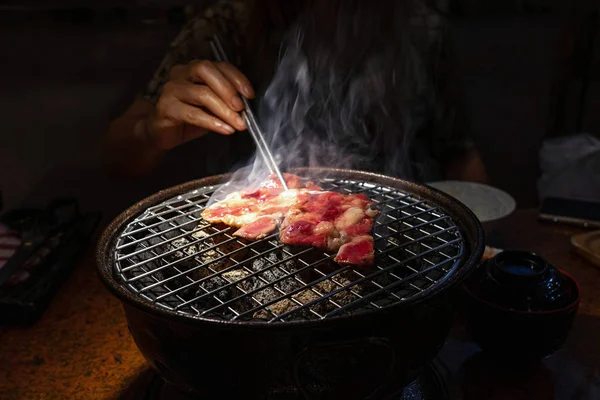 Mano femminile con bacchette che tengono manzo crudo sulla griglia a carbone Fotografia Stock