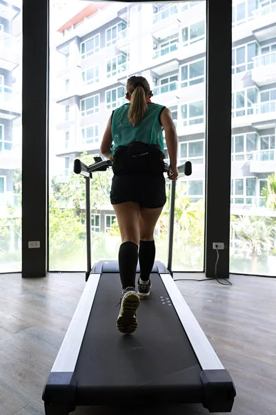 Asian woman jogging on indoor treadmill with building background