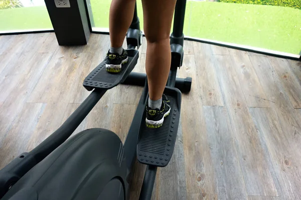 Female legs using elliptical trainer on wooden floor