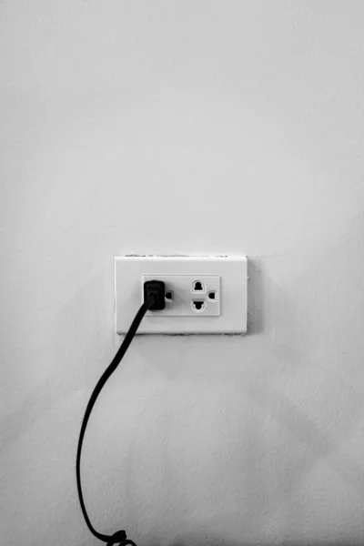 Electrical outlet with black cord connected on white wall — Stock Photo, Image