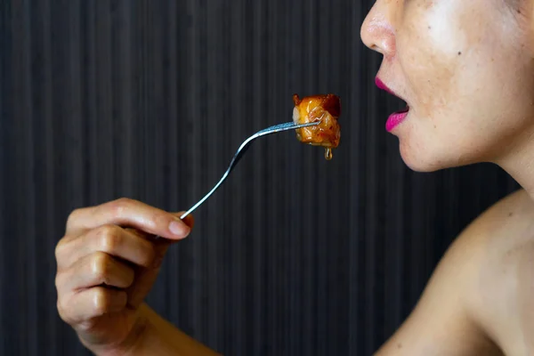 亚洲妇女吃熏肉包装香肠与钢叉 免版税图库照片