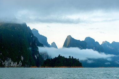 Sabah vakti bulutlar ve sisler kireçtaşı sıradağları üzerinde mavi göl ile Tayland, Surat Thani 'deki Khao Sok Ulusal Parkı' nda..