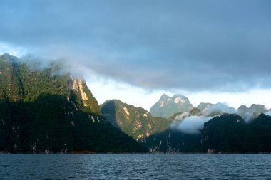 Bulutlar, sis ve sabah ışığı kireçtaşı sıradağları üzerinde. Tayland, Surat Thani 'deki Khao Sok Ulusal Parkı' ndaki göl..