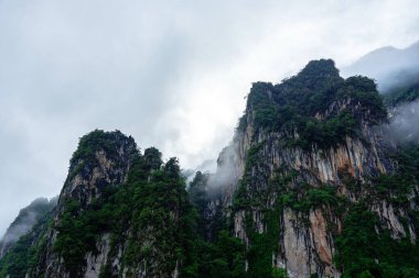 Sabahları ağaçlarla kaplı yüksek kayalık uçurum ve Tayland, Surat Thani 'deki Khao Sok Ulusal Parkı' nda beyaz bulutlar..