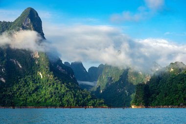 Sabah ışığında yeşil kireçtaşı sıradağları ve Tayland Surat Thani 'deki Khao Sok Ulusal Parkı' nda mavi göl ve gökyüzü bulutları..