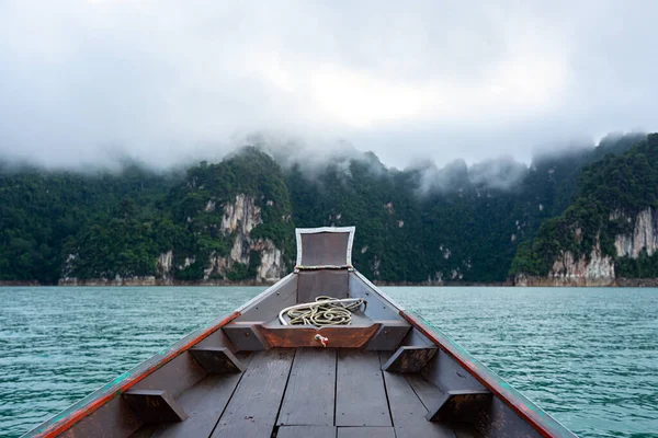 Wooden boat in the lake with morning mist over limestone mountain range background in Khao Sok National Park in Surat Thani, Thailand.