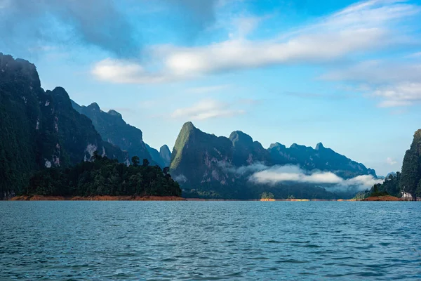 Shadow of limestone mountain range and lake in the morning light with mist and clouds in Khao Sok National Park in Surat Thani, Thailand.