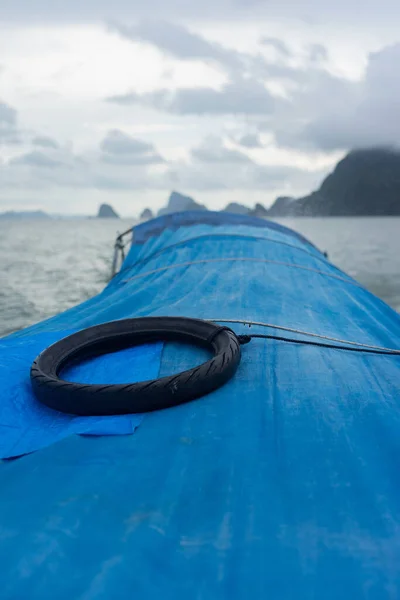 タイのパンガー湾の小さな島と曇りの空の背景と青いボートの屋根の上の黒いタイヤ — ストック写真
