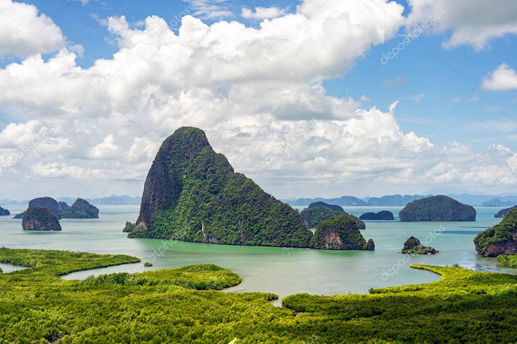 Limestone islands and green mangrove forest with white clouds on blue sky in Phang Nga Bay, Thailand.