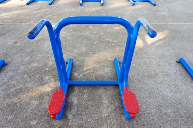 Boş mavi ve kırmızı kamusal egzersiz ekipmanları parktaki beton zeminde.