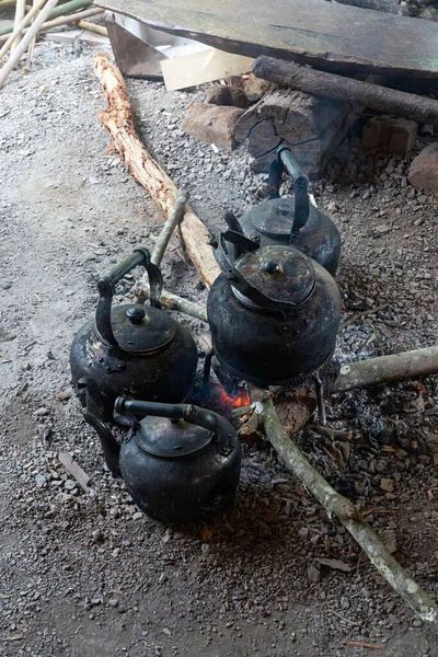 Old kettles with black soot on red bonfire with firewood and ashes.