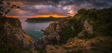 Keskin kayalarla dolu bir körfezin üzerinde gün batımı