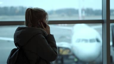 Genç bir kız arkadaş veya akraba havaalanında. Uçuş bekliyor. Cep telefonunuzun terminalde uçuş beklentilerini sırasında konuşurken kız.