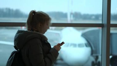 Kalkış için bekleyen ve cep telefonunu kullanarak kadın seyahat. Genç bir kız bir ileti yazar. Uçuş için bekliyor
