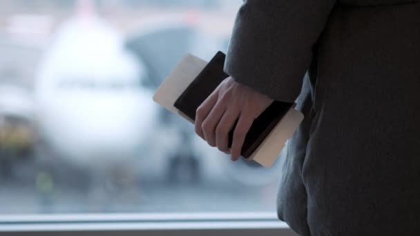 Niña o adolescente con gafas, en una bufanda mirando un avión en el aeropuerto, sosteniendo su pasaporte y billete. Llega tarde y un poco perdida. Disparo de rastreo manual . — Vídeo de stock