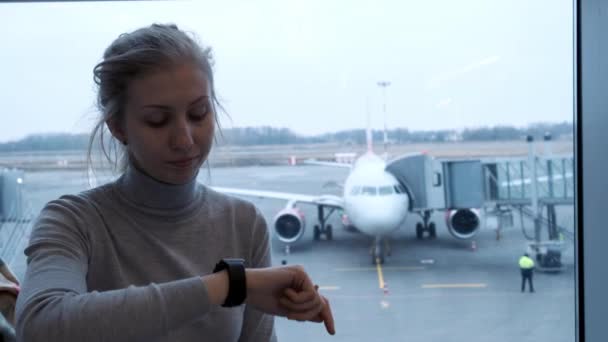 Jonge toeristische vrouw op zoek naar haar vluchtstatus op het bord van de planning en controle tijd op slimme horloges in de luchthaven. 4k. — Stockvideo