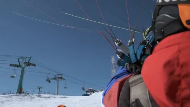 SHEREGESH RUSSIA - 05.04.2018: raises the sail wing of the paraglider. He starts to take off, breaks away from the ground, runs away. Paragliding in winter. — Stock Video