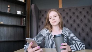 Kafede kahve içme telefon üzerinde app gülümseyen kullanan akıllı kız. Güzel genç casual kadın profesyonel üstünde hareket eden telefon.