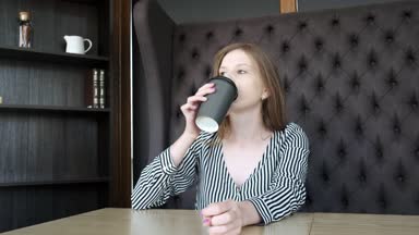 Şık bir kafede güzel bir genç kız işe gitmeden önce sabahları kahve içiyor. Pencerenin oturuyor. Karton siyah cam kahve içiyor. Yakın çekim.