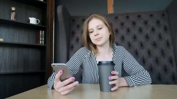 Menina Smartphone usando aplicativo no telefone beber café sorrindo no café. Jovem profissional feminino casual bonita no telefone móvel . — Vídeo de Stock