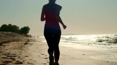 20'li yaşlarda batımında sahilde kum üzerinde çalışan kız. Açık havada koşu.