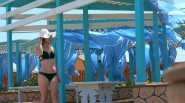 seksi kız yürüyüş bir Açık Yüzme Havuzu. Siyah seksi mayo, beyaz bir şapka ve gözlük. Ağır çekim çekim, perdeleri ve kumaşlar.