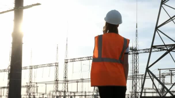 Bir kız mühendisi olarak beyaz bir kask ve bir portakal koruyucu yelek teller ve elektrik ile bir güç istasyonu olup olmadığını denetler. Yeni sahiplik sorunu çözer. — Stok video