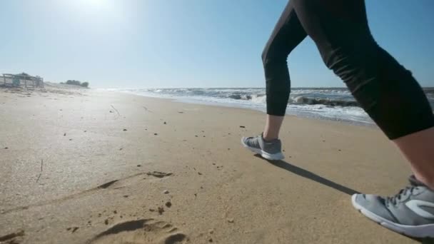 Ein junges Mädchen läuft in roter Sportbekleidung am Strand entlang. hört Musik über Kopfhörer. Joggen am Abend oder Morgen bei Sonnenuntergang oder Sonnenaufgang. — Stockvideo