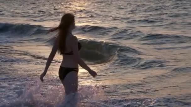 Divatos lány egy fekete fürdőruha belép a tengerre a naplemente. Én vagyok boldog, a tenger és a strand. Tapasztalható a szabadság. Megy a vízbe — Stock videók