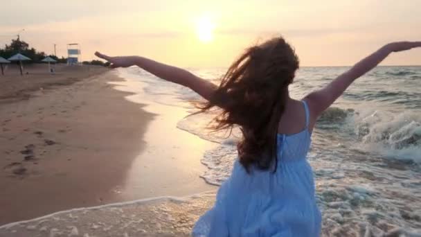 MOCIÓN LENTA: Chica corriendo en aguas poco profundas al atardecer. Una chica vestida de blanco corre por el borde del mar. Estoy feliz con el mar y la playa. Experimentar la libertad . — Vídeos de Stock