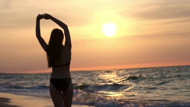 Ein modisches Mädchen in einem schwarzen Badeanzug steigt bei Sonnenuntergang ins Meer. Ich bin glücklich mit dem Meer und dem Strand. Freiheit erleben. geht ins Wasser — Stockvideo