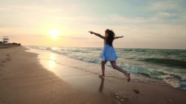 Ağır çekim: sığ suda günbatımında çalışan kız. Beyaz elbiseli bir kız denize yakın kenarında sular çalışıyor. Deniz ve plaj ile mutluyum. Özgürlük karşılaşmış.