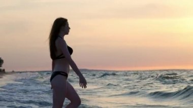 bir siyah mayo moda kız gün batımında denize girer. Deniz ve plaj ile mutluyum. Özgürlük karşılaşmış. Suya gider