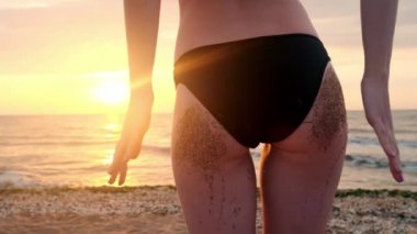 Arka güzel genç kızlar sahil kumu eşek yavaş dize bikini seksi popo tatil tropikal giyen kapalı kapatmak atış görüntüleyin. Kız günbatımı kum kıçından sallıyor.