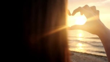 Ağır çekim, Close Up: tanınmayan kadın kalbi ile ayar güneş yakalamak parmak şeklinde. Genç kız aşk elleri altın gökyüzü çarpıcı karşı ve sabah güneş yükselen sembolü yapma