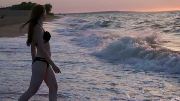 Fashionabla flicka i en svart baddräkt in havet i solnedgången. Jag är nöjd med havet och stranden. Upplever frihet. Går i vattnet — Stockvideo