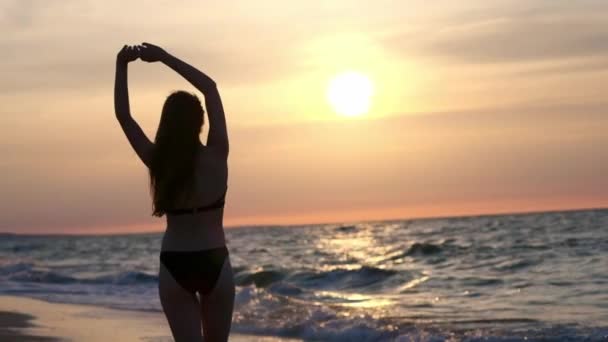 Divatos lány egy fekete fürdőruha belép a tengerre a naplemente. Én vagyok boldog, a tenger és a strand. Tapasztalható a szabadság. Megy a vízbe — Stock videók