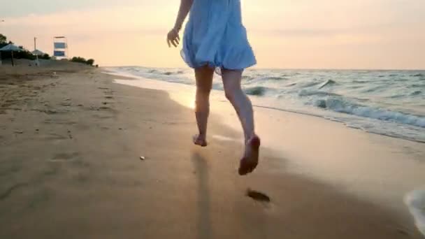 スローモーション: 女の子が夕日で浅い水を実行します。白いドレスの少女は、エッジで水が、海の近くで実行中です。海とビーチと満足しています。自由を経験してください。. — ストック動画