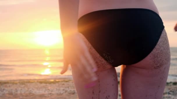 Rückansicht schöne junge Mädchen Strand Sand aus Arsch Zeitlupe tragen String Bikini sexy Po tropischen Urlaub Nahaufnahme. Mädchen schüttelt bei Sonnenuntergang den Arsch aus dem Sand. — Stockvideo