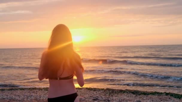 Divatos lány egy fekete fürdőruha belép a tengerre a naplemente. Én vagyok boldog, a tenger és a strand. Tapasztalható a szabadság. Megy a vízbe — Stock videók